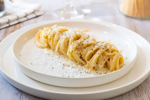 Un plat de tonnarelli cacio e pepe, des pâtes crémeuses saupoudrées de fromage et de poivre noir, sur une assiette blanche.