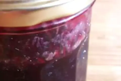 Un pot de confiture de raisin noir, avec des morceaux de fruits visibles, prêt à être dégusté.