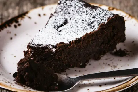 Une part de torta tenerina, un gâteau au chocolat intense, saupoudrée de sucre glace, sur une assiette rustique.