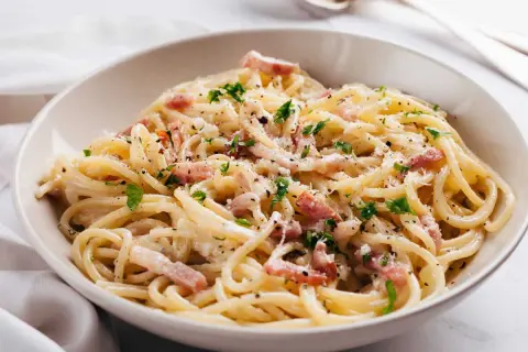 Un plat de carbonara romaine crémeuse, garni de lardons, de persil frais et de parmesan râpé. Un délice !