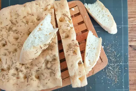 Délicieuse focaccia sans gluten, parsemée de romarin et de sel, coupée en tranches sur une planche en bois.