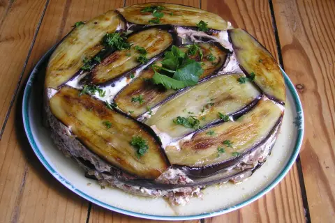 Moussaka ronde, une délicieuse moussaka ricetta, garnie d'aubergines grillées et de persil frais, sur une assiette blanche à bordure verte.