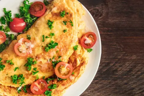 Une savoureuse omelette grecque, garnie de tomates cerises et de persil frais, sur une assiette blanche.