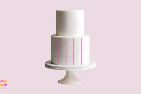Un gâteau blanc à deux étages sur un présentoir, avec des lignes roses indiquant comment faire un gâteau de couche.