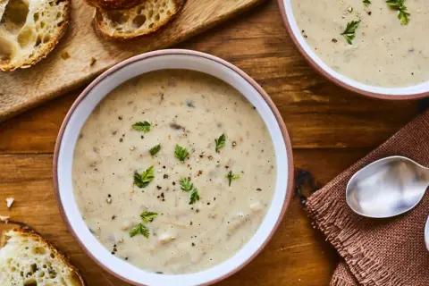 Deux bols de velouté de champignons à la crème, garni de persil et de poivre, avec des tranches de pain croustillant sur une planche en bois.