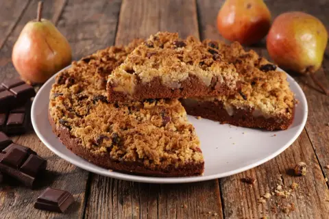 Une délicieuse tarte aux poires, avec une croûte croustillante et des morceaux de chocolat noir, est présentée sur une assiette blanche.