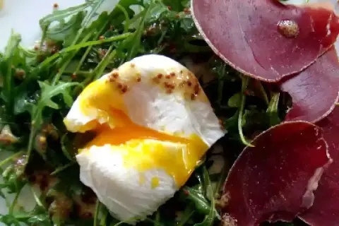 Salade lyonnaise avec œuf poché coulant, roquette et fines tranches de viande séchée.