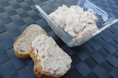 Deux tranches de pain de campagne garnies de rillettes de thon, avec un bol de rillettes de thon en arrière-plan.