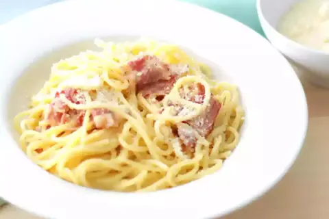Un plat de pâtes à la carbonara crémeuses, garni de lardons croustillants et de parmesan râpé, prêt à être dégusté.