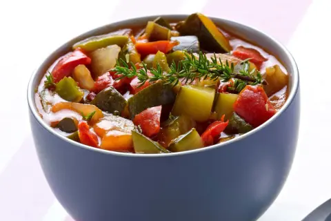 Un bol de ratatouille niçoise, un plat coloré de légumes mijotés, garni d'une branche de thym frais.