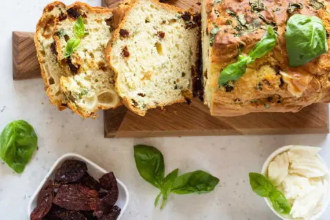 Un délicieux cake salé aux tomates séchées et basilic, parfait pour l'apéro. Des tranches sont coupées, révélant sa mie moelleuse.