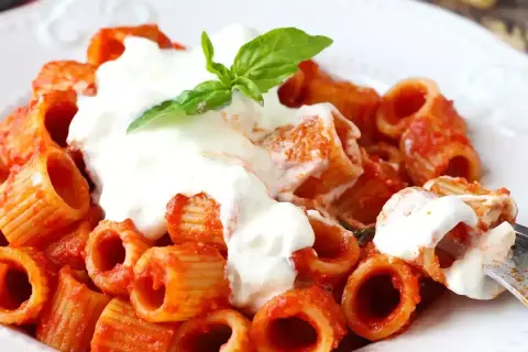 Pâtes rigatoni en sauce tomate, généreusement nappées de stracciatella crémeuse et garnies d'une feuille de basilic frais. Un délice !
