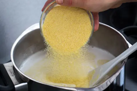 Une main verse de la semoule dans une casserole de lait chaud pour préparer un délicieux semoule au lait.