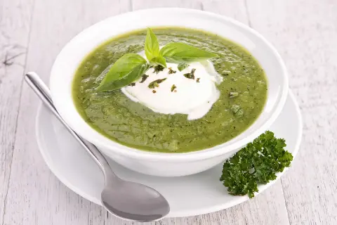 Soupe froide courgette fromage frais, garnie de basilic et persil. Une cuillère repose à côté du bol.