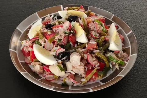 Salade niçoise revisitée avec du riz, garnie d'œufs durs, de thon, de haricots verts, de tomates, de radis et d'olives noires.