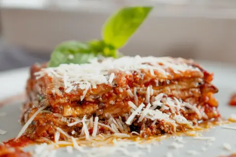 Tranche d'aubergine parmigiana, garnie de parmesan râpé et d'une feuille de basilic frais. Un délice italien.