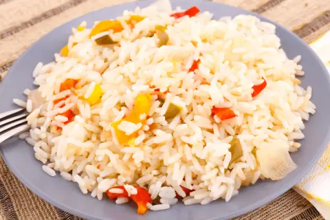 Une assiette de riz créole coloré avec des morceaux de poivrons rouges et jaunes.