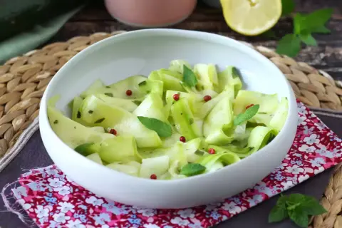 Salade fraîche de courgettes crues marinées au vinaigre, parsemée de baies roses et de menthe.