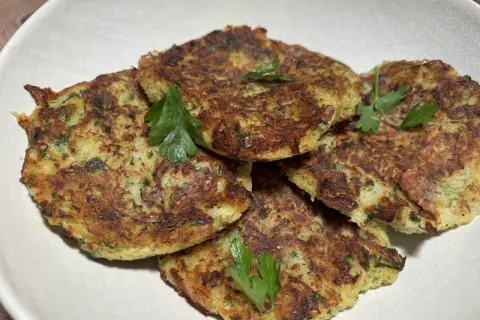 Galettes dorées de courgette et pomme de terre, garnies de persil frais, présentées dans un plat blanc.