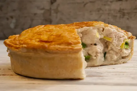 Une tourte au poulet dorée et croustillante, coupée pour révéler une garniture crémeuse et généreuse de poulet et de légumes verts.