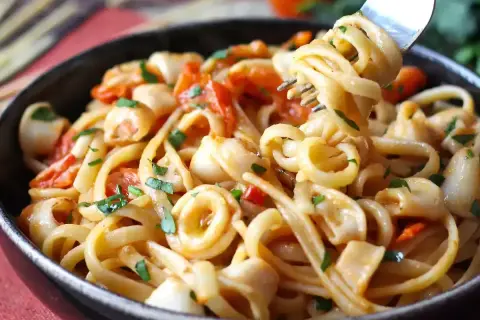 Une assiette de pâtes aux calamars italienne, garnie de persil frais et de morceaux de tomates. Une fourchette soulève une portion de ce plat savoureux.