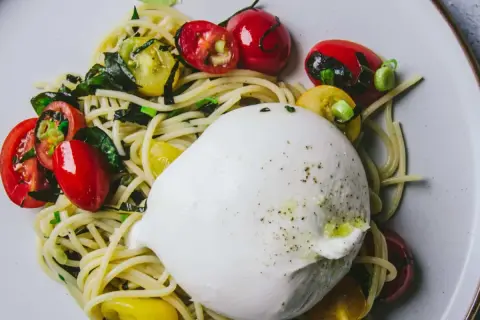 Délicieuse recette avec burrata : pâtes, tomates cerises rouges et jaunes, et herbes fraîches sur une assiette.