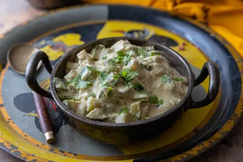 Un plat de courgettes au curry crémeux, garni de coriandre fraîche, servi dans un bol en métal sur un plateau décoré.