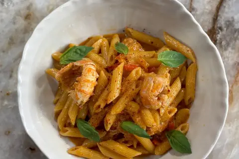 Un plat de pâtes aux langoustines, garni de feuilles de basilic frais et d'une sauce onctueuse. Un délice pour les amateurs de fruits de mer.