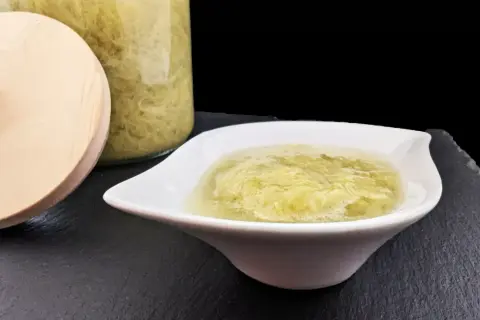 Une coupelle blanche présente une compote de rhubarbe onctueuse, avec un bocal en verre rempli de cette même compote en arrière-plan.