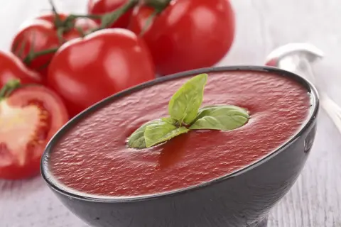 Un bol de soupe de tomates fraîches, garni de basilic, avec des tomates mûres en arrière-plan.