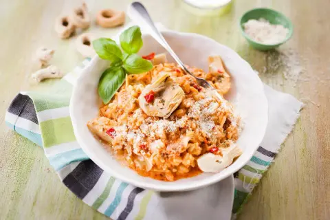 Un délicieux risotto pesto rosso, garni d'artichauts et de basilic frais, saupoudré de parmesan.