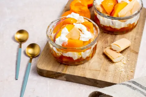Deux coupes de dessert healthy aux pêches et crème fouettée, garnies de biscuits à la cuillère.