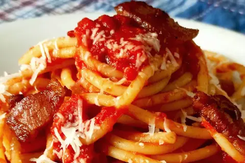 Un plat de pâtes amatriciana, avec des morceaux de guanciale croustillant, une sauce tomate riche et du fromage râpé.