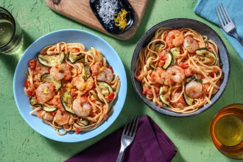 Deux assiettes de linguine crevettes courgettes, garnies de zeste de citron. Un plat savoureux et coloré.