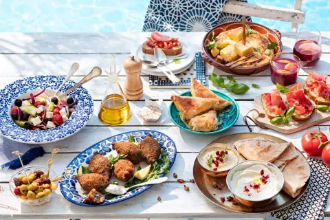 Idée apéro rapide sans cuisson : salade grecque, houmous, pain pita, feuilletés, bruschettas et olives, le tout près d'une piscine.