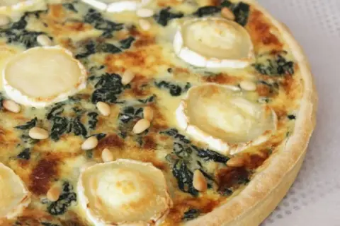 Quiche épinard chèvre, garnie de rondelles de fromage de chèvre et de pignons de pin, prête à être dégustée.