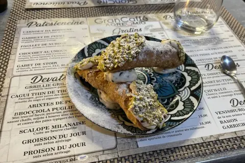 Deux cannoli siciliens garnis de crème et de pistaches concassées, saupoudrés de sucre glace.