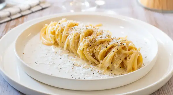 Un plat de tonnarelli cacio e pepe, des pâtes crémeuses saupoudrées de fromage et de poivre noir, sur une assiette blanche.