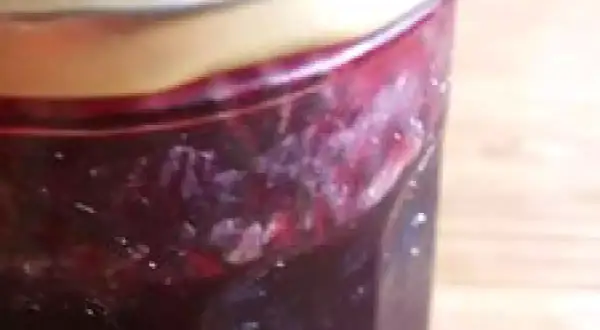 Un pot de confiture de raisin noir, avec des morceaux de fruits visibles, prêt à être dégusté.