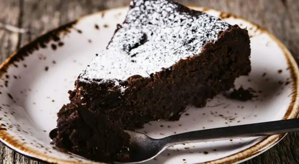 Une part de torta tenerina, un gâteau au chocolat intense, saupoudrée de sucre glace, sur une assiette rustique.