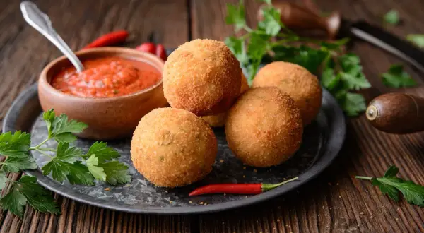 Arancini dorés et croustillants, accompagnés de sauce tomate et de piment. Une recette parfaite pour un apéritif gourmand.