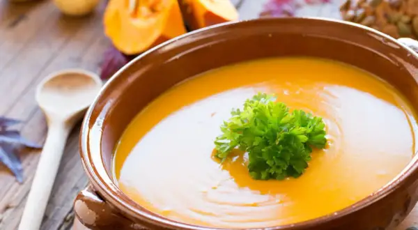 Soupe potimarron onctueuse, garnie de persil frais, dans un bol en terre cuite. Des morceaux de potimarron et une cuillère en bois complètent cette scène automnale.