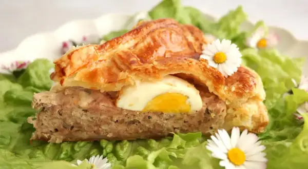 Tranche de pâté de Pâques savoureux, garni d'un œuf dur, sur un lit de salade verte et décoré de pâquerettes.