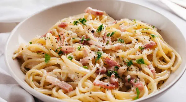 Un plat de carbonara romaine crémeuse, garni de lardons, de persil frais et de parmesan râpé. Un délice !