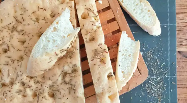 Délicieuse focaccia sans gluten, parsemée de romarin et de sel, coupée en tranches sur une planche en bois.