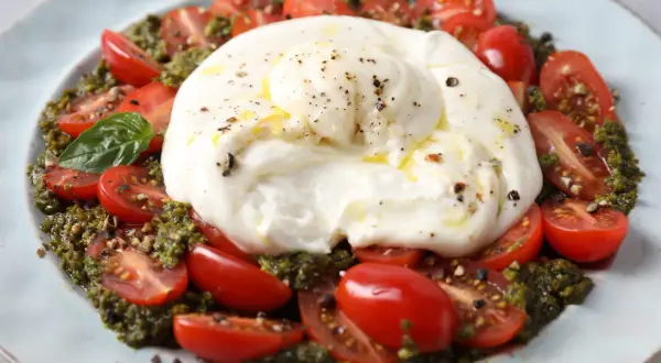 Une délicieuse recette burrata froide avec des tomates cerises coupées, du pesto et une touche de poivre noir.
