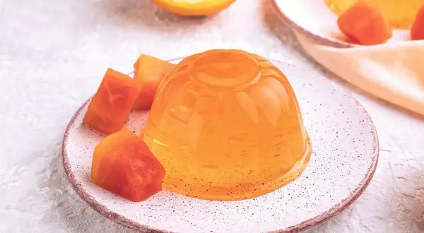 Une gelée orange brillante, servie avec des morceaux de fruits, parfaite pour apprendre comment faire de la gelée maison.