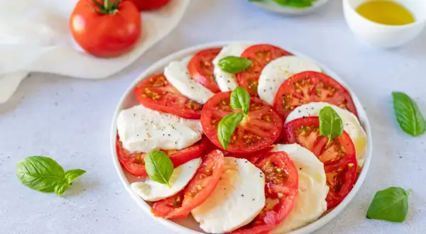Salade Caprese al limone : rondelles de tomates fraîches, mozzarella crémeuse et feuilles de basilic, assaisonnée d'un filet d'huile d'olive.