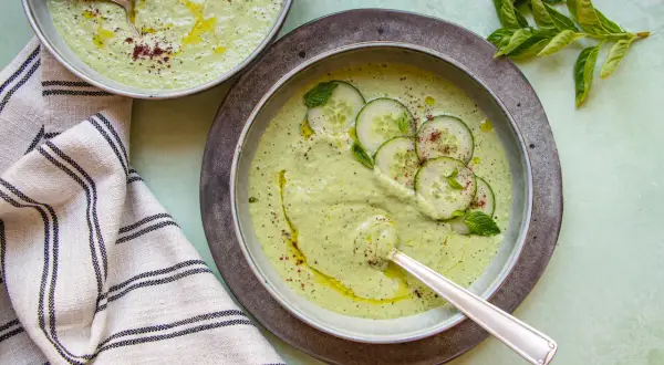 Deux bols de soupe froide crémeuse aux concombres, garnie de rondelles de concombre, de menthe et d'un filet d'huile d'olive.