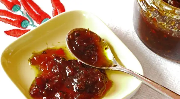 Une cuillère sert une délicieuse confiture de piment, avec un bocal et des piments rouges brodés en arrière-plan.